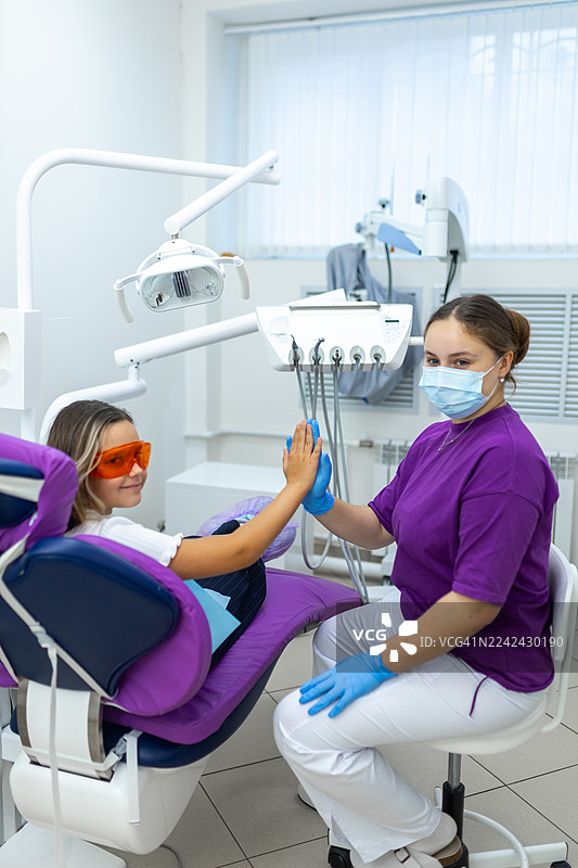 友好的牙科就诊：儿童患者在明亮的诊所里与牙医击掌图片素材