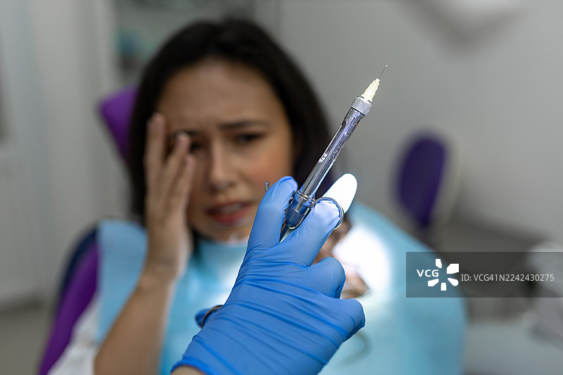 一位焦虑的病人正准备接受注射，一位戴着手套的牙医正拿着注射器图片素材