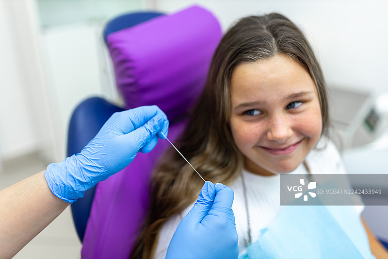 年轻患者在牙科检查时微笑，戴着手套的牙医正准备为牙齿进行牙线清洁图片素材
