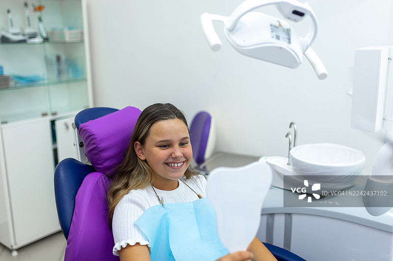 快乐的孩子在牙科诊所里，坐在明亮现代的椅子上，戴着防护围兜，在检查时露出笑容图片素材