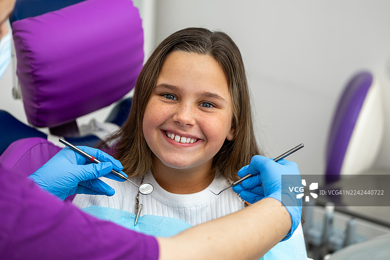 牙医诊所里，一位面带微笑的小女孩正在接受友好的检查，医护人员关怀备至。图片素材