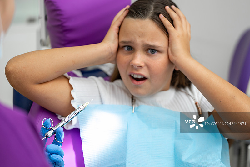 一个小女孩在牙医诊所，她感到焦虑和害怕，因为现场有注射器和牙科器械。图片素材