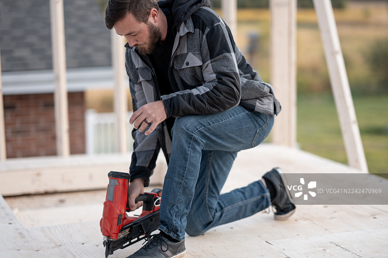 装修期间，一名男子在建筑工地使用钉枪组装木制框架。图片素材