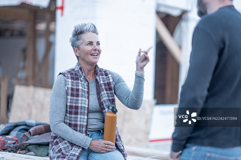 自信的中年女士，灰发，身穿格子背心，在建筑工地讨论项目图片素材