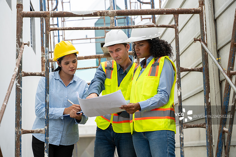 工程师和建筑师们身着安全背心和头盔，在建筑工地进行检查，审视建筑结构，讨论项目蓝图和使用平板电脑进行施工管理，身处安全工业环境中。图片素材