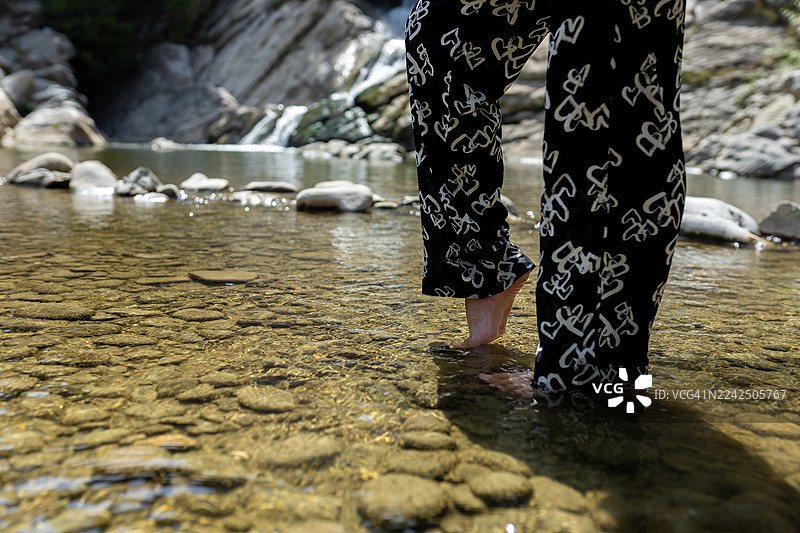穿着印有白色心形图案的黑裤子，赤脚走在浅浅的河水中探索大自然图片素材