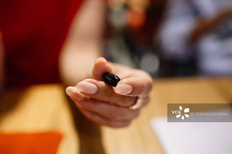 一只手在木桌上拿着一颗黑色小药丸，暗示着维生素或补充剂图片素材