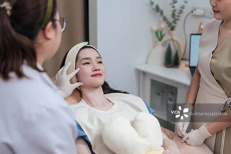 亚洲女性患者在治疗前咨询医生关于面部改善的问题。皮肤科医生在现代美容诊所检查女性皮肤，为美容治疗做准备。图片素材