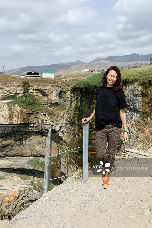 一位女子站在达吉斯坦悬崖小径旁，附近有瀑布和峡谷的风景图片素材