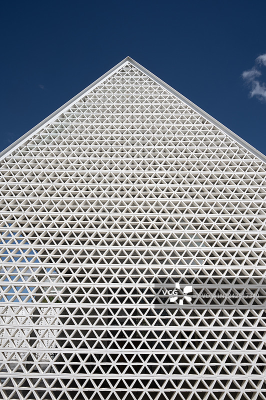 一座现代三角形建筑立面，饰有重复的白色三角形几何格栅图案，背景为晴朗的蓝天。图片素材