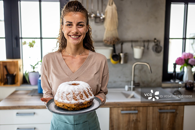 面带微笑的女士在明亮现代的厨房里展示撒了糖粉的磅蛋糕，适合家庭烘焙图片素材
