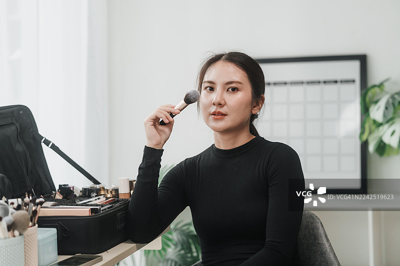 亚洲女专业化妆师肖像，在工作室摆姿势，手持化妆刷，展现出职业自信、魅力和艺术感。图片素材