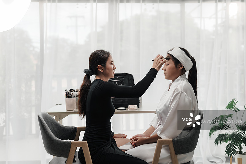 专业美容师为新娘化妆，准备婚礼当天。化妆品应用。化妆师在工作室工作场所为女性客户化妆。图片素材