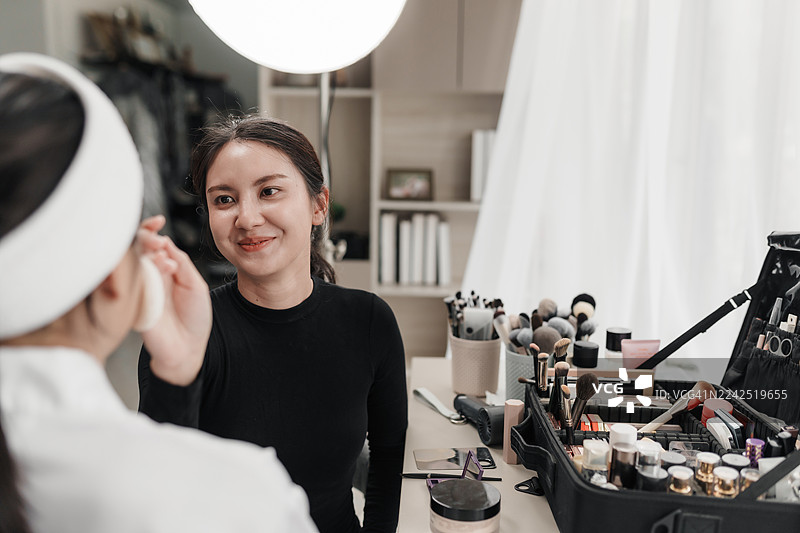 化妆师在时尚工作室为客户涂抹粉底化妆品。打造迷人的时尚生活方式的专业准备。化妆师专注于护肤和完美底妆。图片素材
