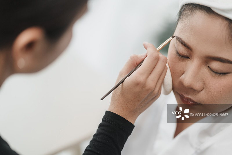 亚洲新娘接受美容师的专业眉毛造型。为婚礼日做准备。化妆。美容师工作和眉毛塑形。图片素材