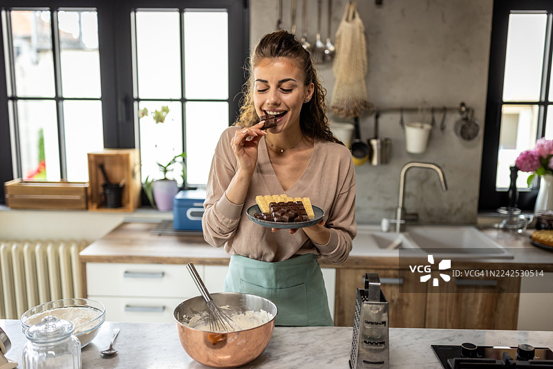 一位女士在现代厨房享用巧克力威化饼甜点，在家烘焙和烹饪图片素材