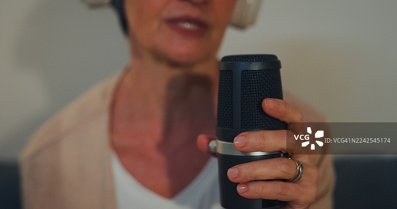 一位戴着头巾的年长女性癌症患者，在家中夜晚的客厅沙发上，戴着耳机通过播客讲述她抗癌康复的故事。癌症生存概念。图片素材