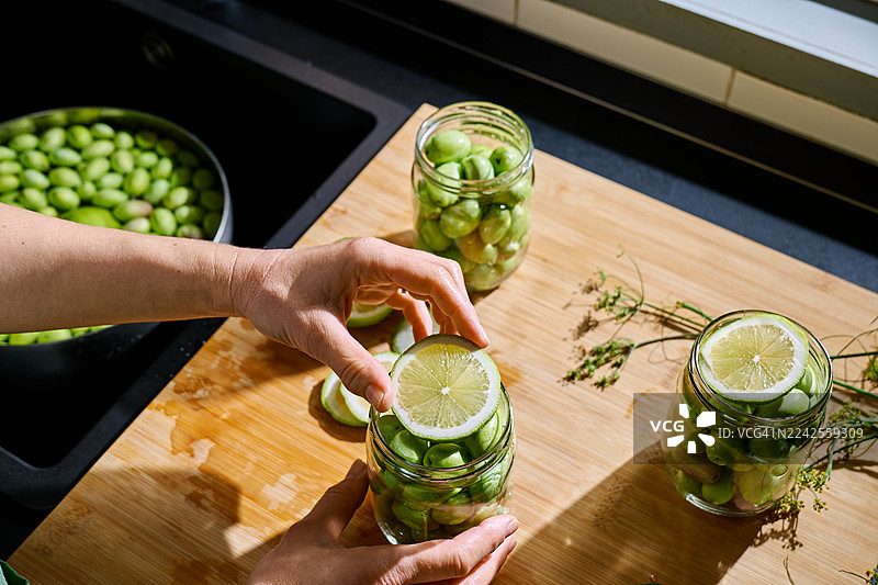 女性双手将柠檬片放入盛满绿色橄榄的玻璃碗中图片素材