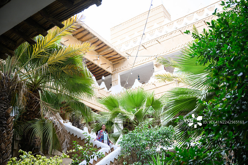 一位身着阿巴亚（Abaya）的女性游客在阿卜哈老城区探索古老的阿拉伯建筑图片素材