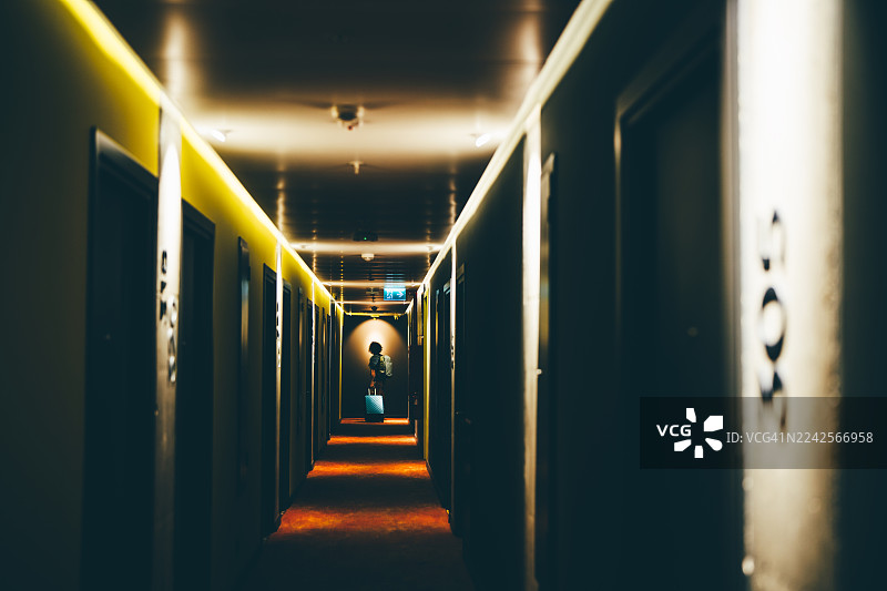 一名男子提着行李走在酒店走廊里。图片素材