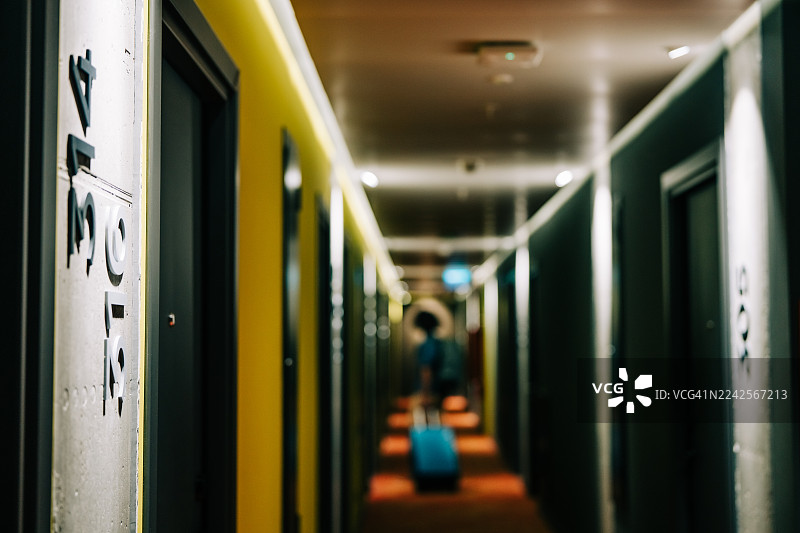 一名男子提着行李走在酒店走廊里。图片素材