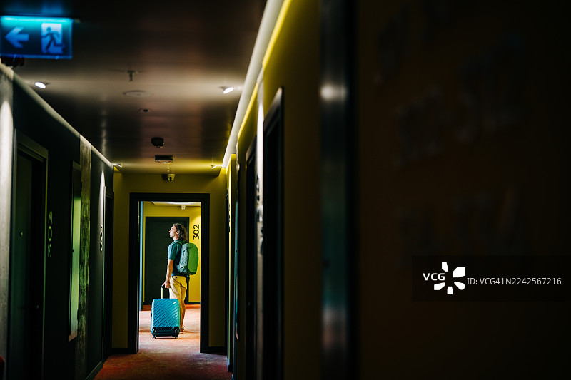 一个男人带着行李走在酒店走廊里。图片素材