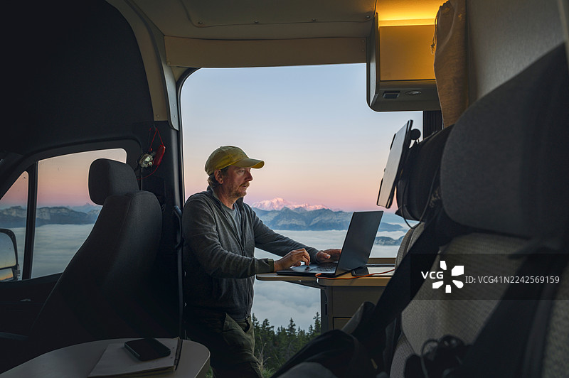 夕阳时分，一位成熟的男士在法国阿尔卑斯山停车，处理一些工作邮件。图片素材