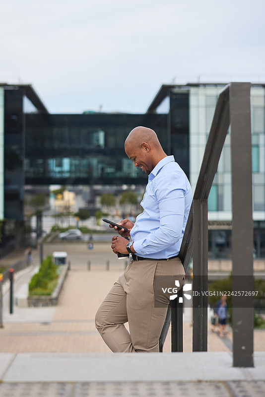 身着商务休闲装的专业黑人男性在现代办公室附近使用智能手机图片素材