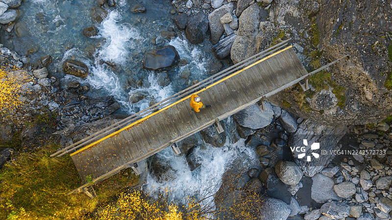 从高空航拍/无人机视角拍摄，一名无法辨认身份的人走在横跨法国阿尔卑斯山脉一条美丽山涧的桥上。图片素材