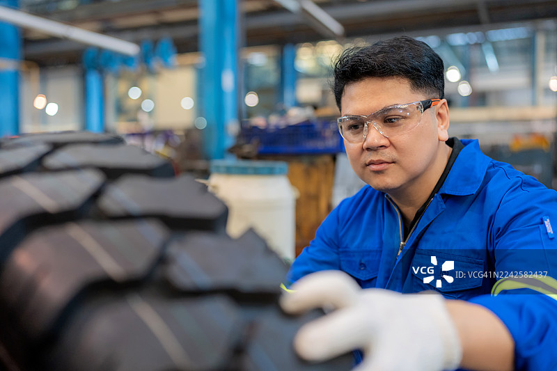 在仓库里，一名身穿安全装备的维修技术人员正在检查轮胎，以验证其质量和是否适合车辆更换，突显了汽车维修和保养过程中的精准、安全和高效。图片素材