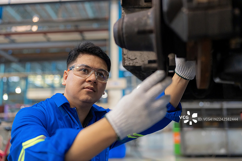 一位身穿安全手套的维修工程师在汽车修理店检查车轮轴和轴承部件。该机械师在重新组装轮胎前进行质量控制，体现了车辆维修的精确性、专业性和安全性。图片素材