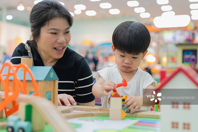 亚洲家庭中的母亲和儿子在室内游乐场/儿童俱乐部/游乐园里，兴高采烈地玩着玩具城市模型汽车，促进亲子关系、感官发展、思维和STEM解决方案的解决，体现了他们的生活方式图片素材