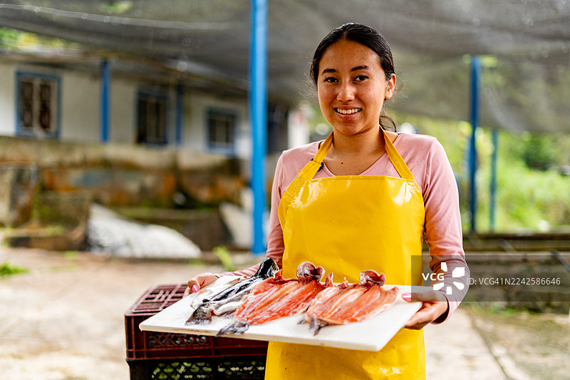 在桑坦德省皮耶德昆斯塔的一个养鱼场，一名十几岁的女孩肖像，她手里拿着新鲜的鳟鱼。图片素材