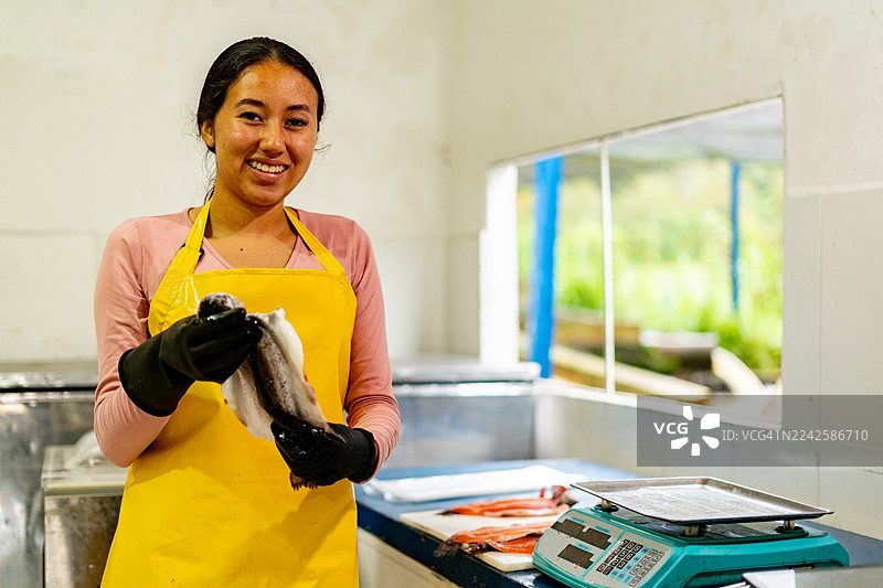 在鳟鱼养殖加工厂，一位少女正在称量鱼的肖像图片素材