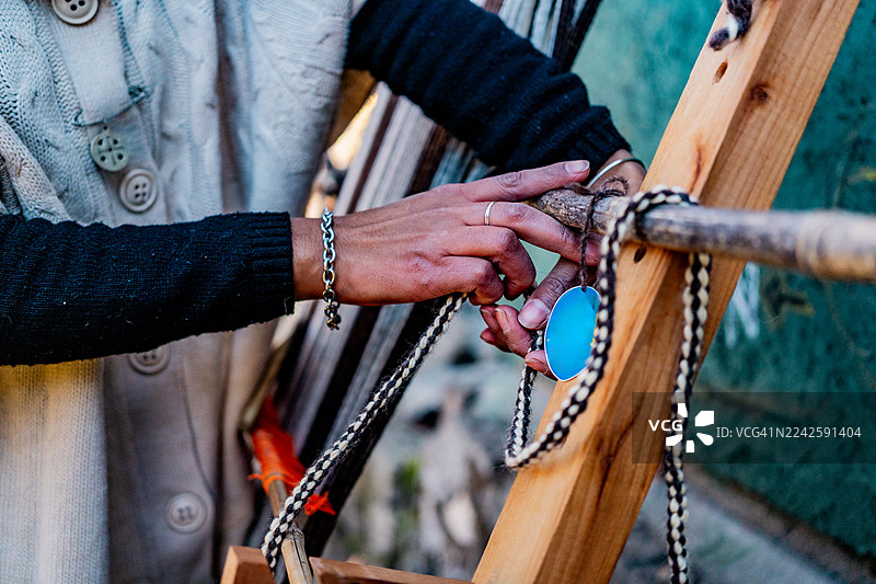 阿根廷圣马丁德洛斯安第斯地区，一位马普切妇女正在使用织布机制作传统披肩的特写图片素材