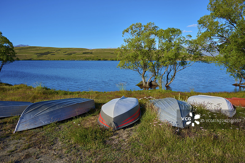 湖岸边倾覆的船只,背景是晴朗的天空和绿色的树木,麦格雷戈湖,蒂卡波,坎特伯雷,南岛,新西兰图片素材