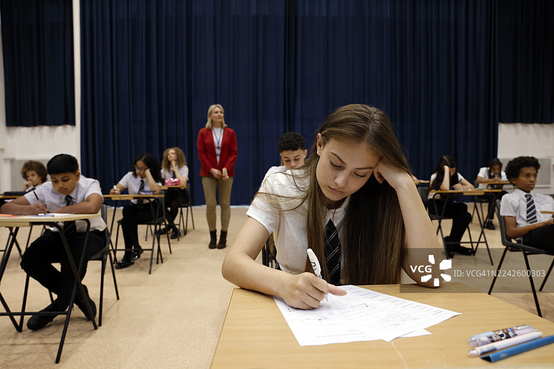一名女中学生在一间宽敞的学校礼堂参加考试，在安静的学习环境中专注于试卷。图片素材