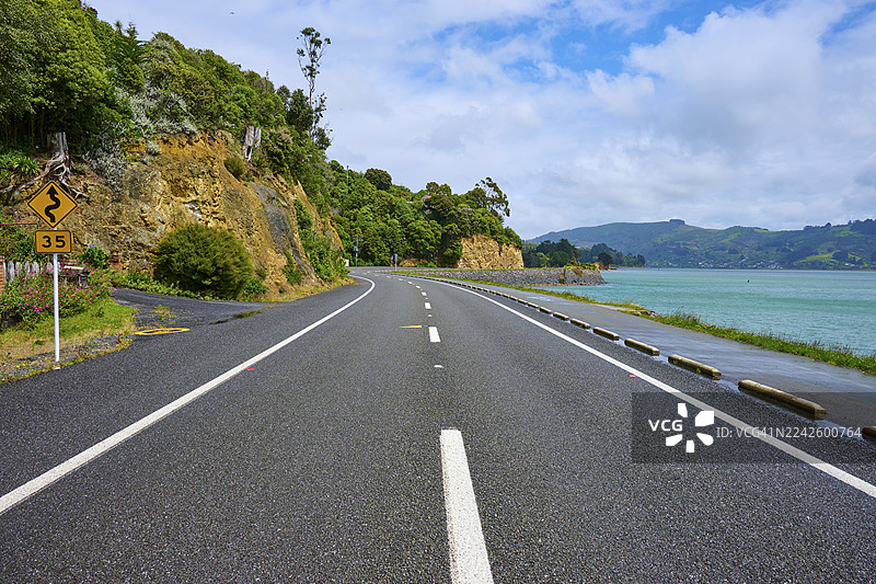 新西兰南岛但尼丁奥塔哥布罗德湾沿海公路，两侧有绿色植被和岩石图片素材