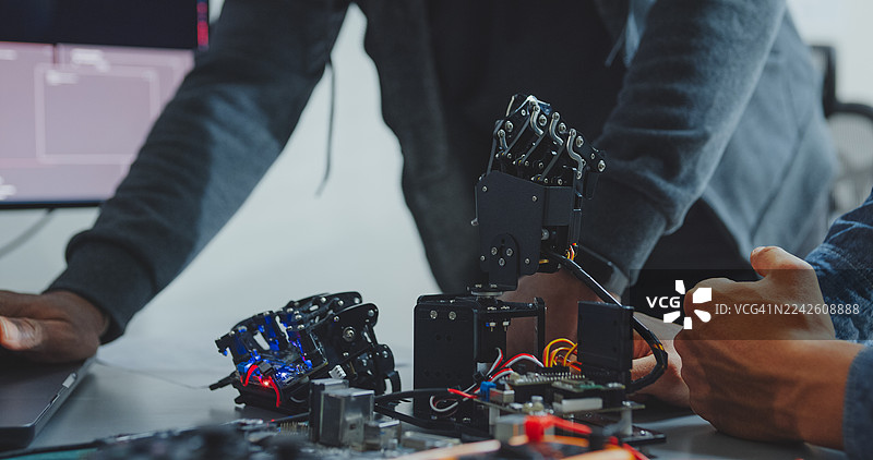 特写镜头：黑人和西班牙裔男性工程师程序员在科技办公室合作开发机器人手原型，使用电脑控制机器人手臂电路。软件开发人员，人工智能。图片素材