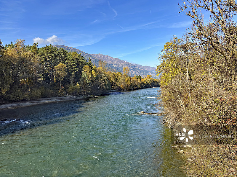 秋季树木和山峦环绕的宁静河流，在晴朗的蓝天下，德劳河，德劳自行车道，利恩茨，蒂罗尔，奥地利图片素材