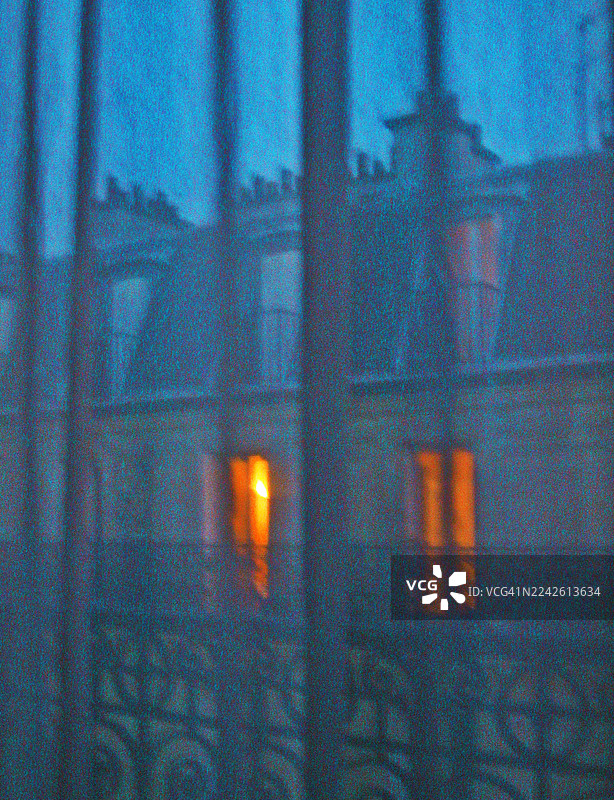 透过另一扇窗户的蓝色窗帘看去，巴黎被灯光照亮的窗户。图片素材
