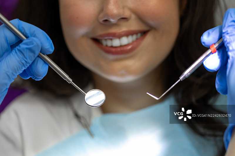 戴着手套的双手和牙科器械在微笑的患者近旁，进行牙科检查的场景图片素材