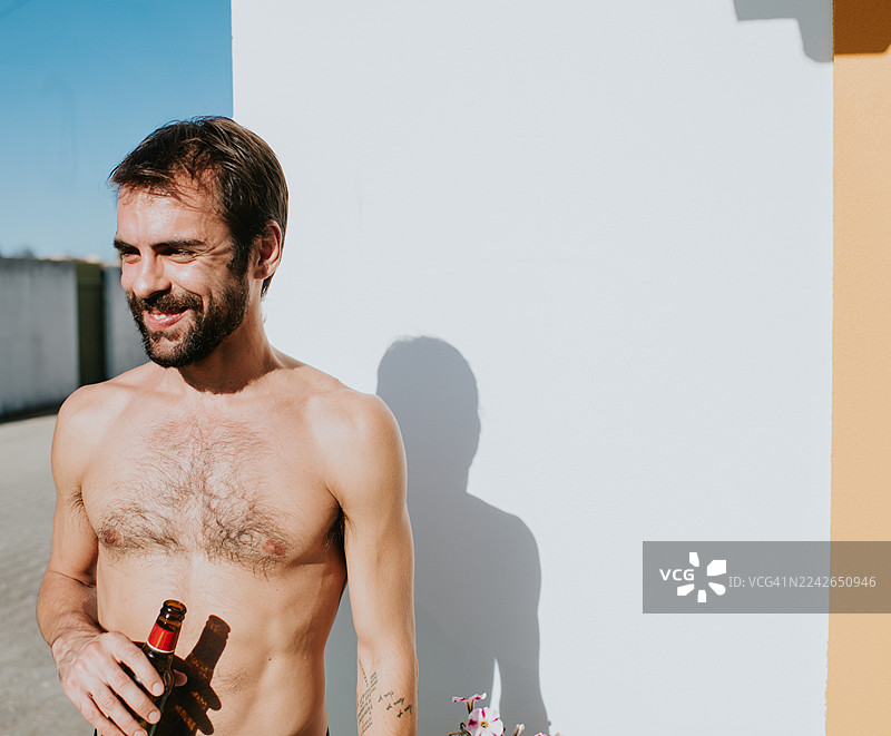 阳光明媚下，男子手持啤酒瓶，面带微笑图片素材
