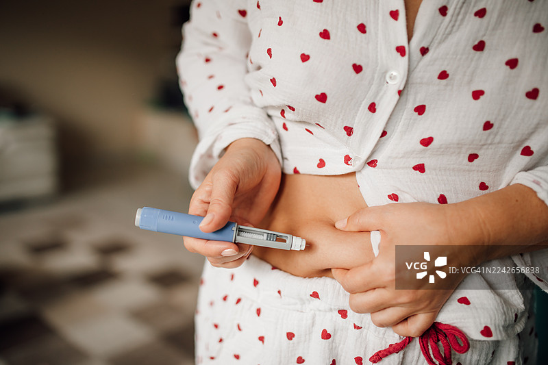 女性在家中用蓝色胰岛素笔向腹部注射胰岛素，糖尿病治疗和日常医疗流程概念图片素材