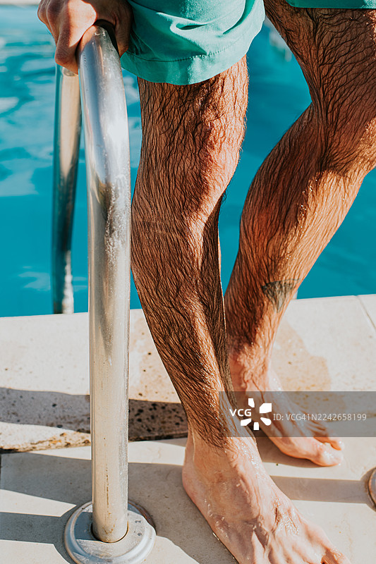 特写：一名男子从游泳池中走出，皮肤和泳裤上水珠滴落图片素材