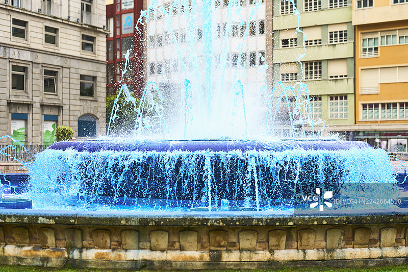 城市广场上喷溅着蓝色染料水的水景喷泉图片素材