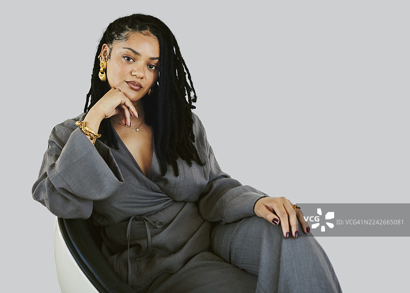 自信的非洲裔美国女性，身着灰色套装，放松地坐在椅子上，进行肖像拍摄图片素材