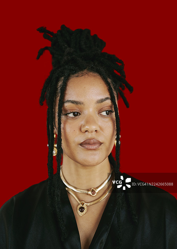自信的非洲裔美国女性，留着脏辫，戴着金饰，身处红色背景肖像图片素材