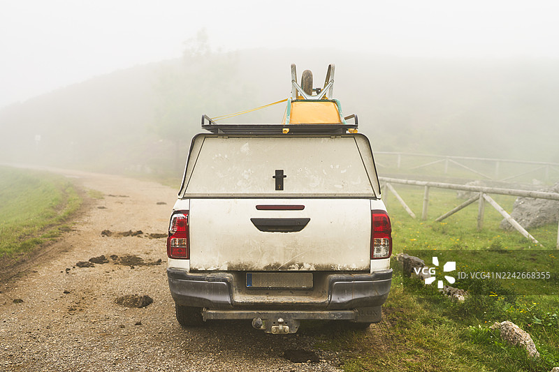 雾气笼罩的乡村土路上停着一辆载有独轮车的皮卡车图片素材