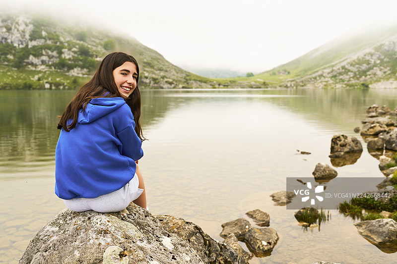 少女坐在山间湖泊旁的岩石上图片素材